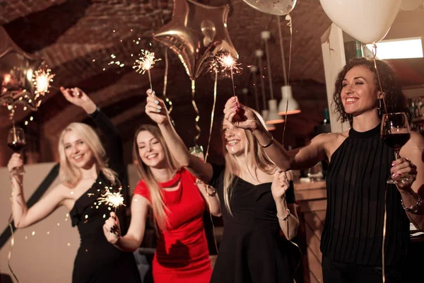 Groep van gelukkig lachend vriendinnen dragen van avondjurken viering van Nieuwjaar houden wonderkaarsen in ingerichte café — Stockfoto