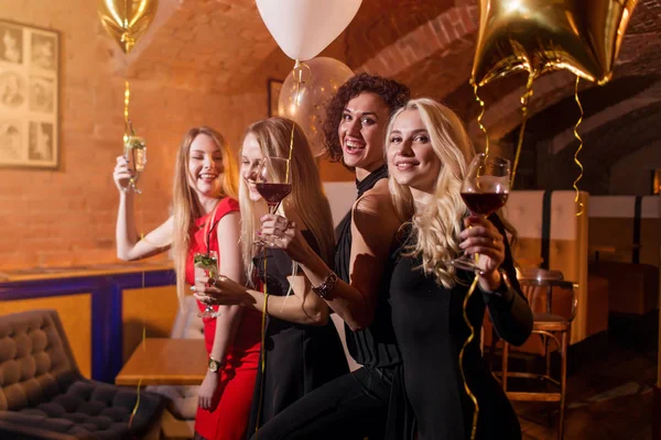 Portret van aantrekkelijke goed geklede jonge vrouwen met glazen alcoholische dranken lachen met plezier op de party in café — Stockfoto