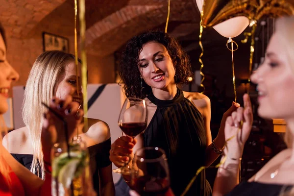 Primer plano de positiva hermosa amigas levantando copas de vino para feliz evento sentado en restaurante de moda —  Fotos de Stock