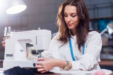 Dikiş makinesi bir atölyede çalışan genç kadın moda tasarımcısı
