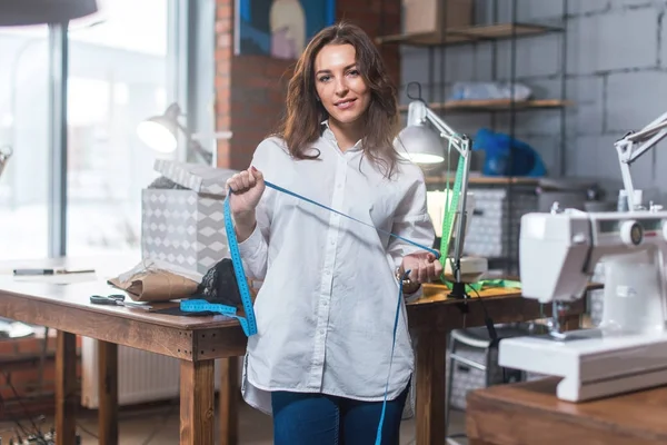 Portrait of pretty brunette fashion designer smiling, looking at camera standing in a sewing workshop against tools and equipment — Stock Photo, Image