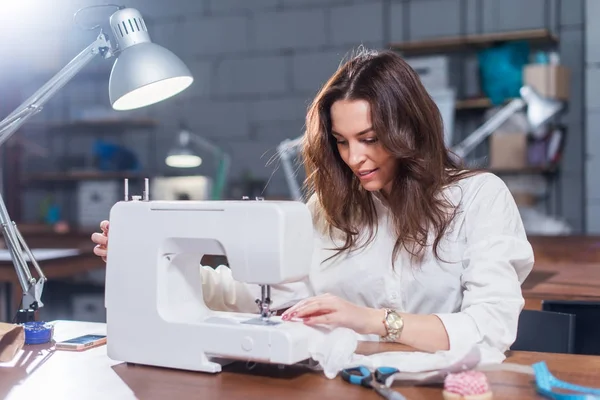 Attractive Caucasian seamstress working stitching with sewing machine at her workplace in studio loft interior — Stock Photo, Image