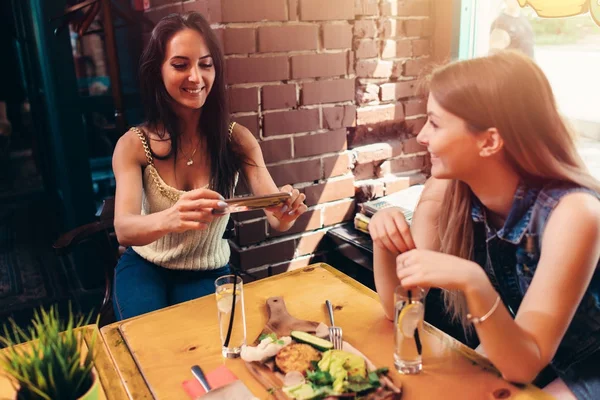 Dos novias almorzando sanas en el café. Mujer joven tomando fotos de comida con teléfono inteligente publicando en las redes sociales — Foto de Stock