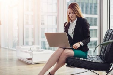 Kadın baş ekonomisti modern ofis koltukta oturan dizüstü kullanarak veri çözümleme