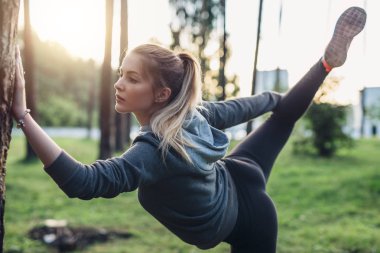 Kadın atlet bacak tutun poz germe egzersiz üzerinde duran bir ayağımı Şehir Parkı yapıyor