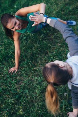 Eller dokunmadan duruş, Vasisthasana, pratik Yoga tarafında duran çimenlerin üzerinde iki mutlu kadın plank