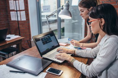 Modern stüdyoda oturup dizüstü kullanarak resimleri izlerken bir müşteri ile çalışan kadın iç tasarımcı