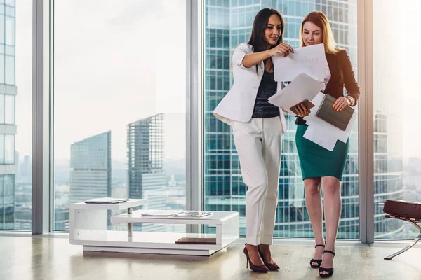 Female businesswomen wearing formal outfit discussing documents standing in office hallway