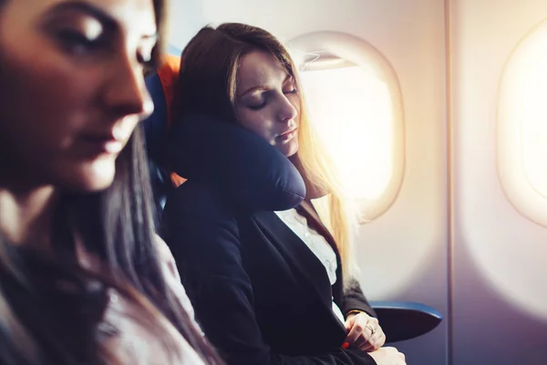 Two businesswomen sleeping in the airplane using neck cushion while going on business trip — Stock Photo, Image