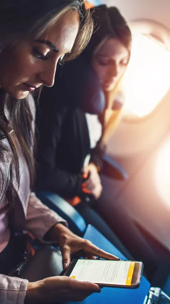 Jonge vrouw werkt, met behulp van een smartphone tijdens het vliegen in een vliegtuig. — Stockfoto