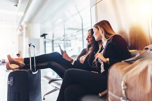 Due signore d'affari guardando il telefono cellulare in attesa del volo nel terminal internazionale dell'aeroporto — Foto Stock