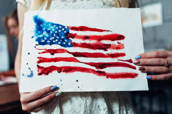 Close-up view of female hands holding a sheet of paper with a hand-darwn watercolor illustration of the flag of the United States — Stock Photo, Image