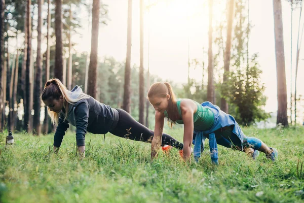 Two female friends doing push-up exercise training outdoors in forest — Stock Photo, Image