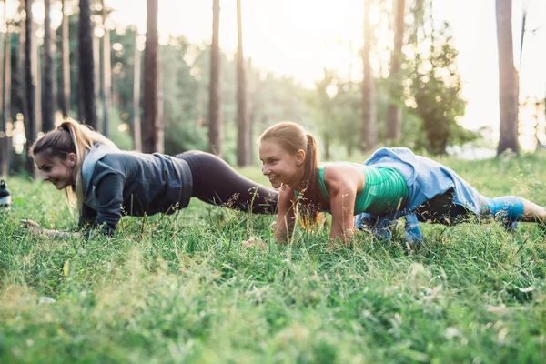 Две девушки тренируются на свежем воздухе, выполняя упражнения на траве — стоковое фото