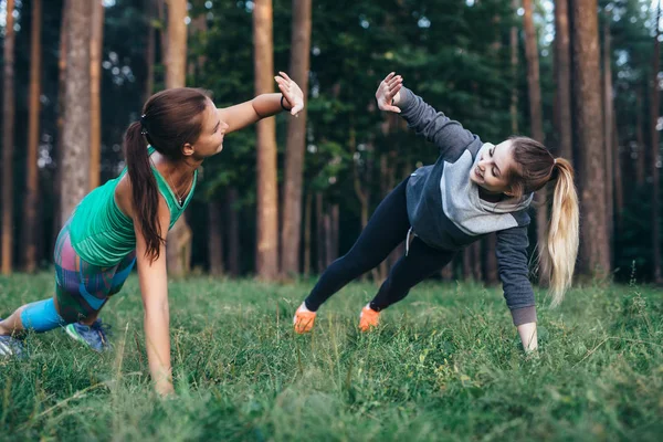 Två kvinnliga kompisar gör partner sida plank ger hög fem medan utbildning i skogen — Stockfoto