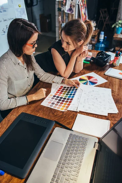 Dizüstü bilgisayar, renk şemaları ve bir kavram seçerek yeni bir proje tartışırken bazı çizimler ile masa başında oturan genç kadın grafik tasarımcıları — Stok fotoğraf