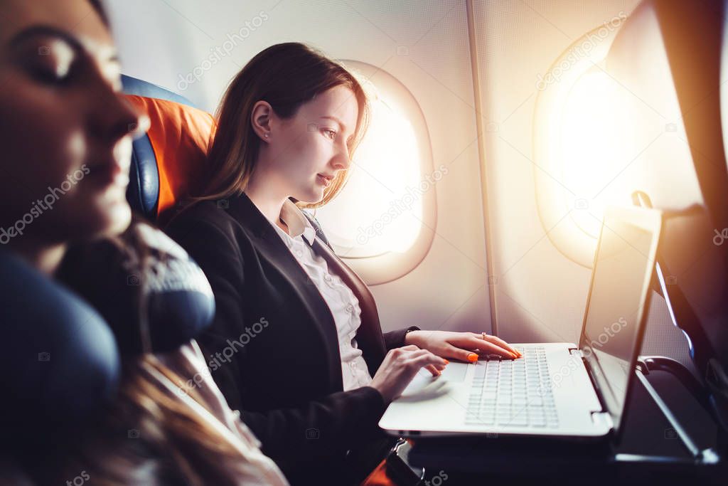 Female entrepreneur working on laptop sitting near window in an airplane