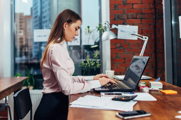 Jovem mulher vestindo roupas formais trabalhando em laptop digitando e-mails sentados em seu local de trabalho — Fotografia de Stock