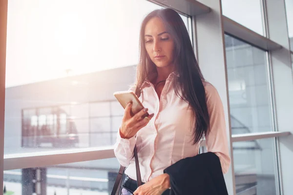 Портрет молодой предпринимательницы, использующей смартфон во время прогулки в зону посадки в аэропорту — стоковое фото