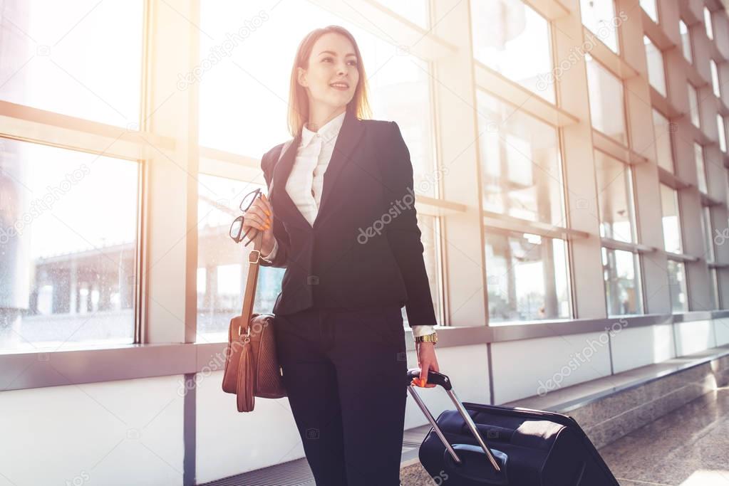 Pretty smiling female flight attendant carrying baggage going to airplane in the airport