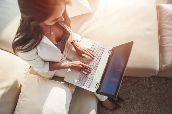 Vista superior de la mujer sentada en un sofá con una computadora portátil en su regazo escribiendo en el teclado en casa —  Fotos de Stock