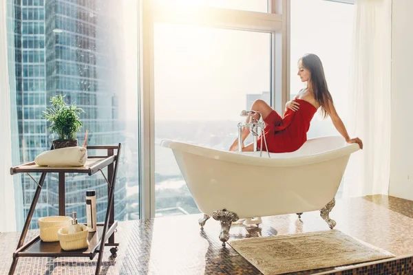 Slanke jonge vrouw in de handdoek zit op bad in de luxe badkamer — Stockfoto