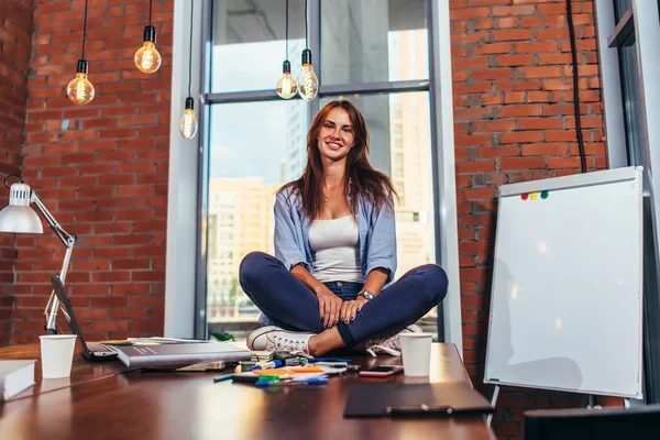 Porträt einer lächelnden Studentin, die auf einem Tisch im Klassenzimmer sitzt — Stockfoto