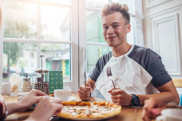 Tyylikäs teini yllään lautasliina tilalla veitsi ja haarukka valmis syömään pizzaa istuu ikkunaa vasten ravintolassa — kuvapankkivalokuva