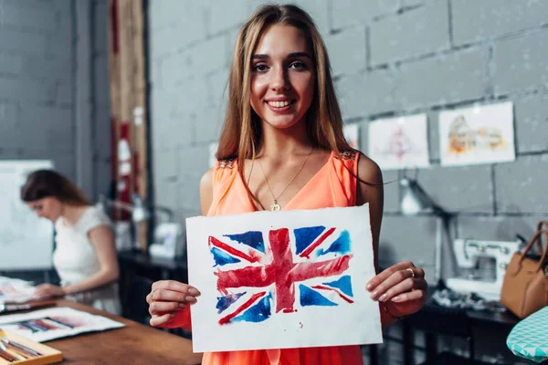 Happy young woman holding a picture of British flag drawn with watercolor technique during art therapy for adults — Stock Photo, Image