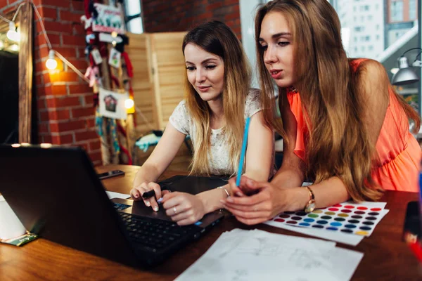 Dvě mladé ženy pracují na nové kreativní design pomocí přenosného počítače diskusi o myšlenky na útulné stylové studio — Stock fotografie