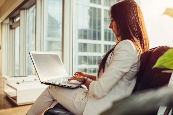 Sidovy av kvinnlig chef bär snygg elegant vit kostym hålla laptop i knäet arbetar i moderna kontors — Stockfoto