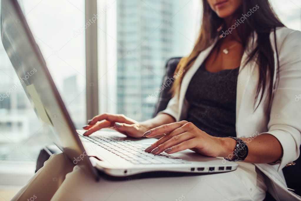 Close-up view of elegant female journalist writing an article using netbook sitting in modern office