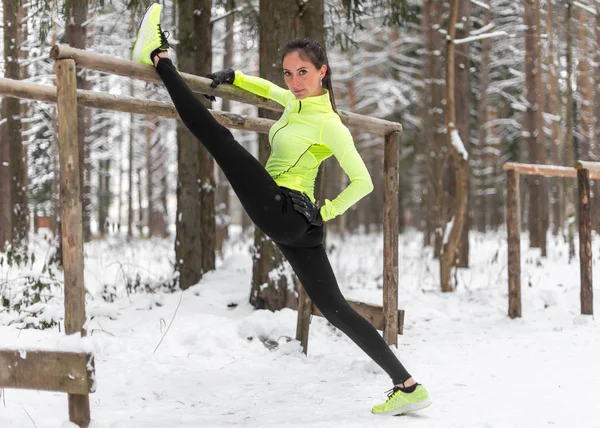 Mulher atleta ajuste fazendo perna esquerda dividir exercícios de alongamento ao ar livre na floresta. Modelo esportivo feminino exercitando parque de inverno ao ar livre — Fotografia de Stock