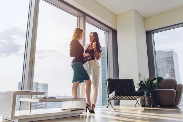 タワー ブロックの現代オフィスに立って計画を議論する 2 つの女性のビジネス パートナー — ストック写真