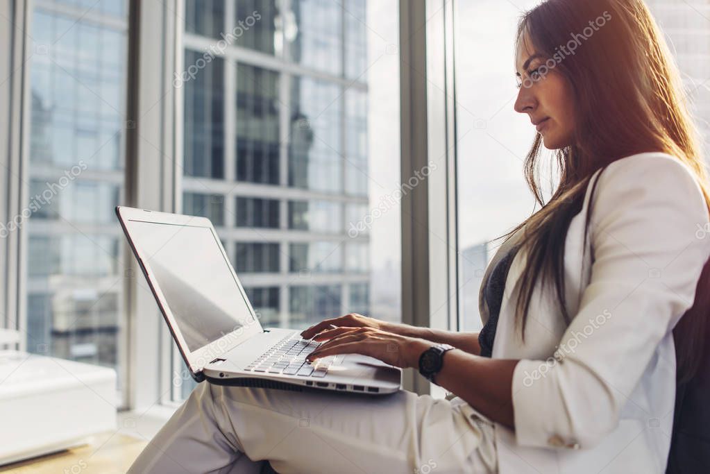 Side view of confident female entrepreneur using laptop sitting in modern business center