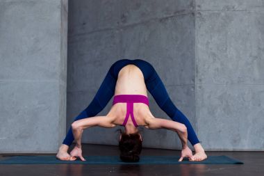Sportif genç kadın ayakta çifte ileri bend poz, Prasarita Padottanasana, working-out kapalı yapıyor yoga uygulamak tam uzunlukta önden görünümü