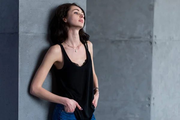 Skinny unga europeiska kvinnliga modellen i casual kläder poserar stående avslappnat lutad mot väggen tittar bort från kameran — Stockfoto