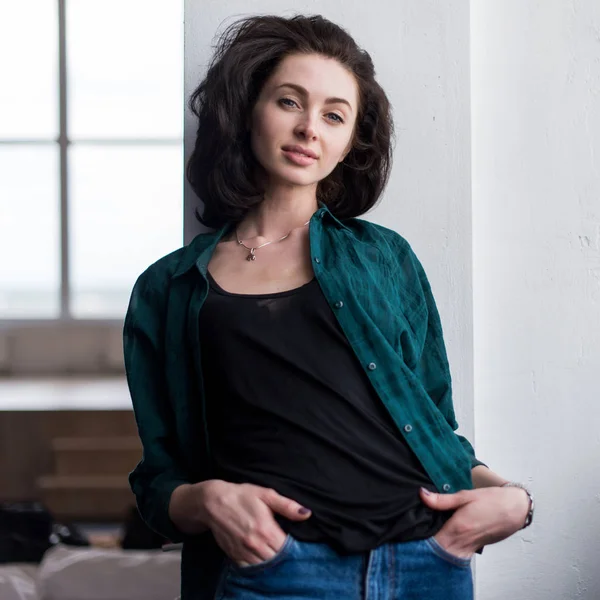 Porträt einer hübschen lächelnden jungen Frau in übergroßer stylischer Teenie-Kleidung, die mit der Hand in Jeanstaschen an der Wand steht — Stockfoto