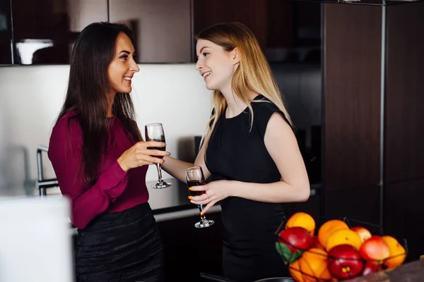 Дві подружки в елегантному одязі розслабляються після покупки, п'ють вино, сміються і пліткують на кухні — стокове фото