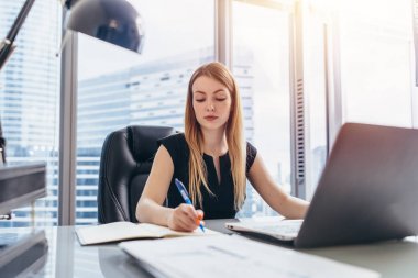 Notlar kalemle yazma ve modern ofis binası içinde bilgisayarını kullanarak randevu alarak onun masasında oturan kadın CEO