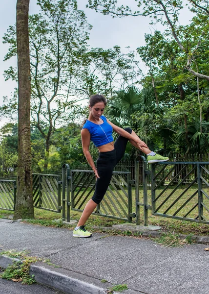 Fit girl dělá protahovací cvičení na plotě v parku. Atletka Příprava na ranní cvičení nebo běhání v létě. — Stock fotografie