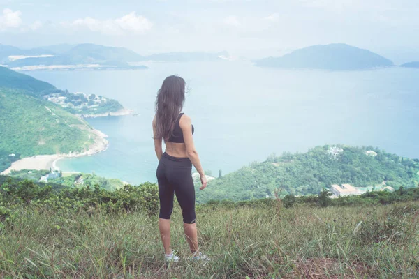 햇빛에 녹색 산과 바다의 전망을 감상 하는 언덕에 서 있는 발랄 한 젊은 여자 — 스톡 사진