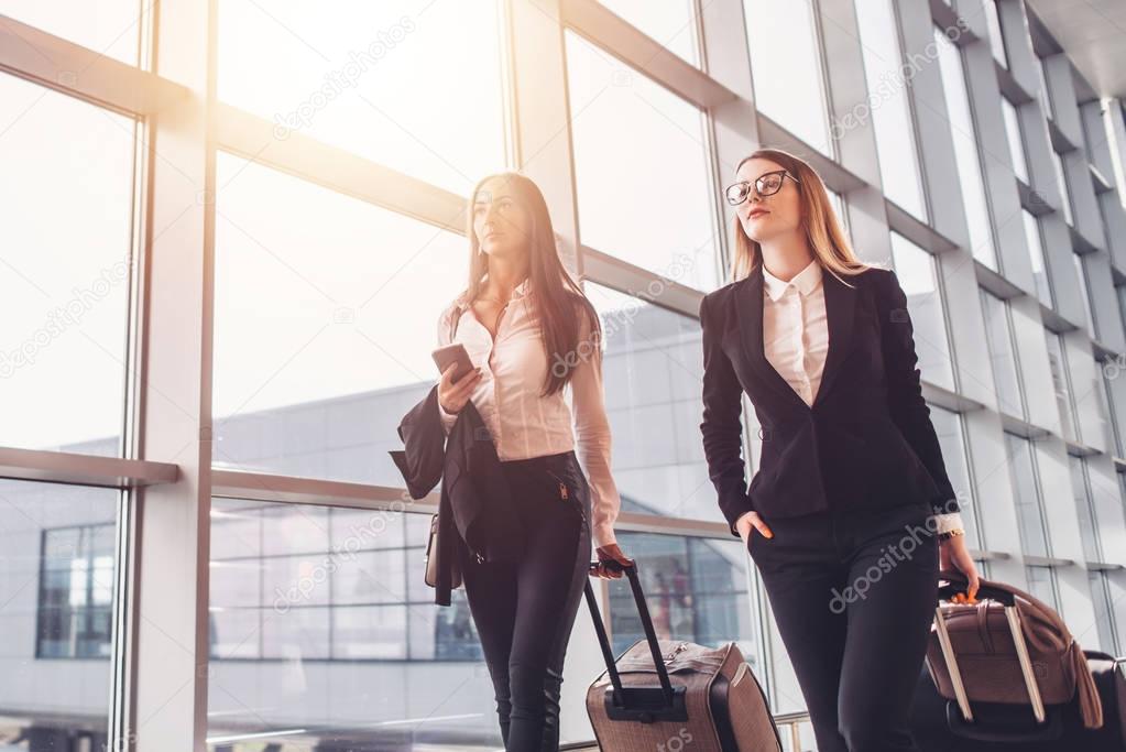 Two confident businesswomen carrying suitcases in airport