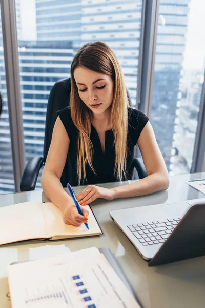 Geconcentreerde zakenvrouw werken schrijven nota's in laptop zitten aan de balie in kantoor — Stockfoto