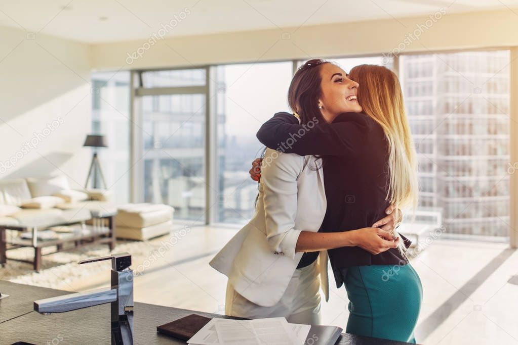 Two girlfriends happy to see each other hugging and laughing standing in loft apartment