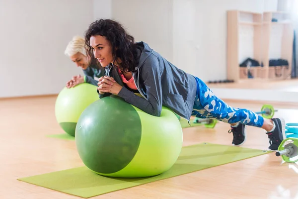 Zwei positive Frauen beim Plankentraining liegend auf Balance-Ball im Fitnessstudio — Stockfoto
