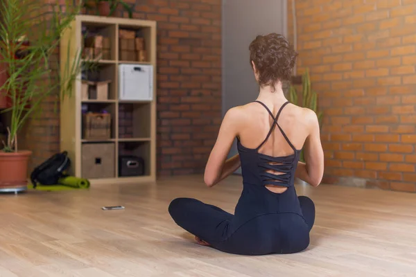 Rückansicht einer Frau, die in Yoga-Lotus-Pose sitzt, entspannt und meditiert im Wohnzimmer — Stockfoto