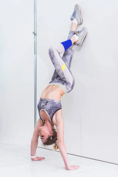 Unga sportiga kvinnor gör handstående övning. Atletiska flickor står i avancerade nedåtriktad tree pose lutad mot väggen under yogaklass inomhus — Stockfoto