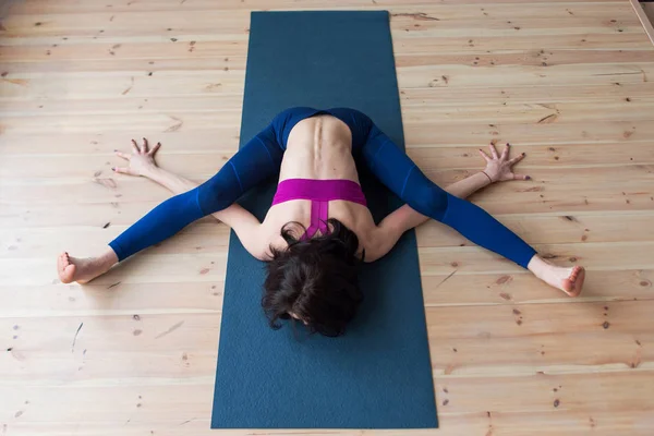 Top view of female yogi doing advanced kurmasana turtoise pose on mat indoors while practicing yoga — стоковое фото