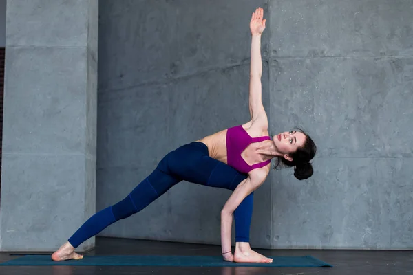 Slim fille caucasienne debout dans la pose d'angle latéral, parsvakonasana, pendant sa routine de yoga dans la salle de gym — Photo